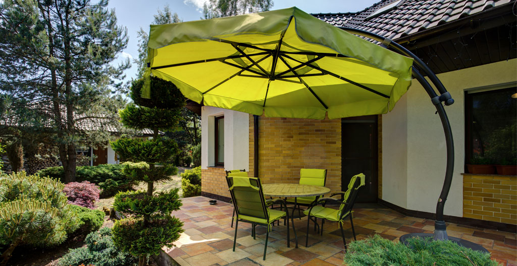 Illustration 3D isométrique montrant une table de jardin rectangulaire vue du dessus avec un parasol circulaire semi-transparent au-dessus, matérialisé par des lignes de cotation indiquant le diamètre de 3m et le débord de 50cm, avec cercles concentriques au sol visualisant les zones de couverture.